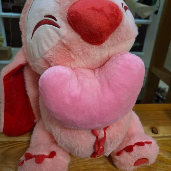 Pink plush teddy bear holding a heart pillow