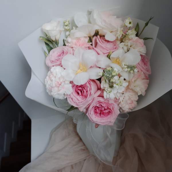Pink and white bouquet of roses and small white flowers wrapped in paper