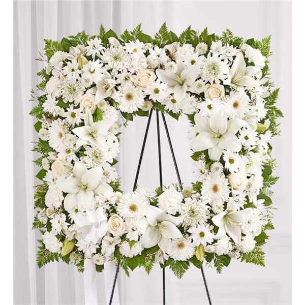 White floral wreath on a black easel with lilies and daisies