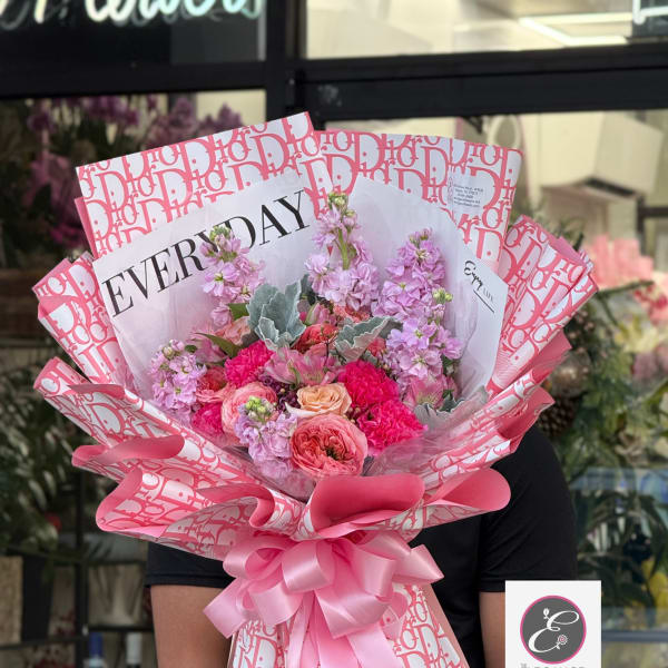 Pink bouquet with roses and ruffled blooms wrapped in patterned paper and ribbon