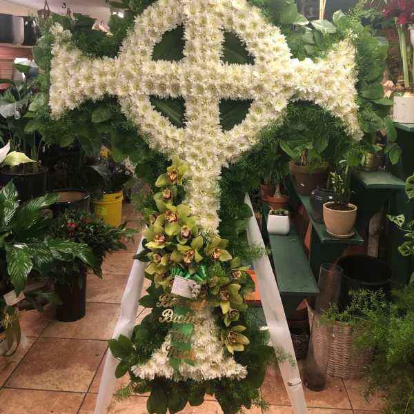 Large white floral cross on an easel with green orchids at the base