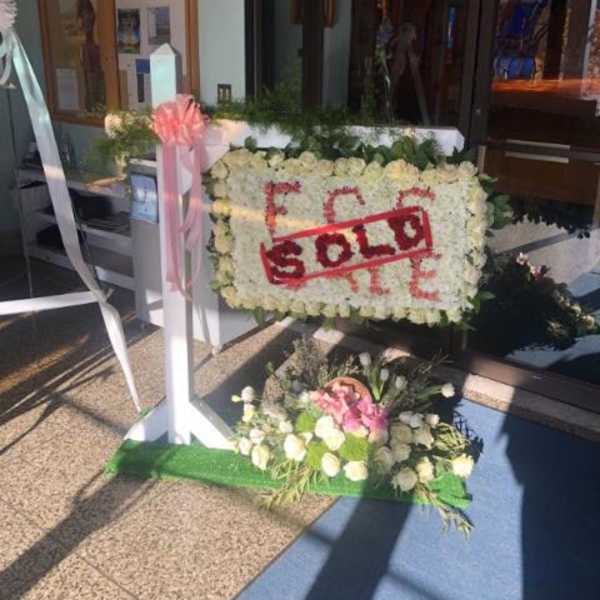 White floral standing sign with a red "SOLD" banner and pink ribbon