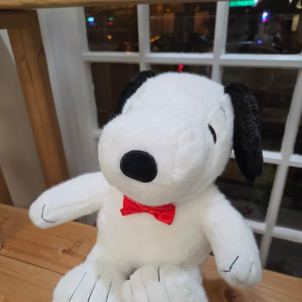Plush Snoopy toy with a red bow tie sitting on a pink box