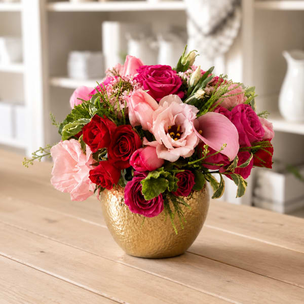Pink and red flower arrangement in a gold vase