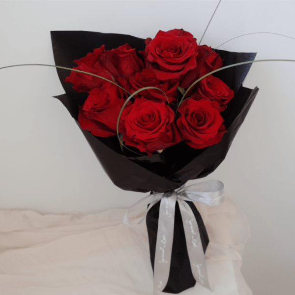 Bouquet of red roses wrapped in black paper with a white ribbon