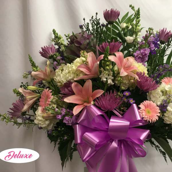 Large bouquet of pink lilies, purple flowers, and white hydrangeas with a purple bow