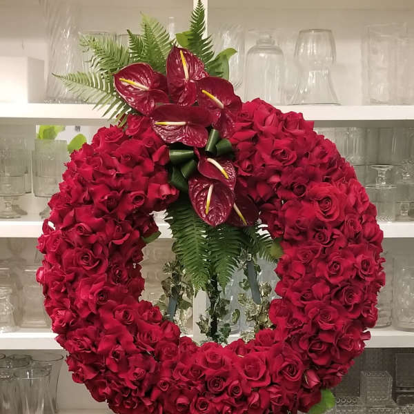 Heart-shaped red rose wreath on a standing easel with anthuriums and fern