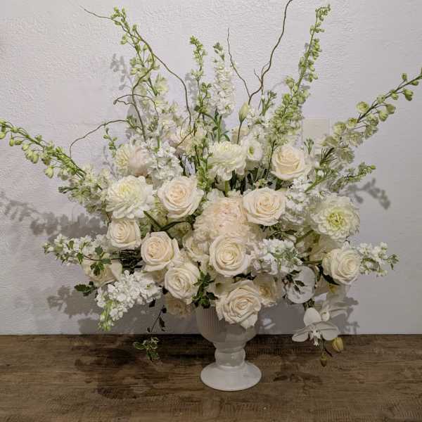 White floral arrangement in a white pedestal vase with tall branching stems