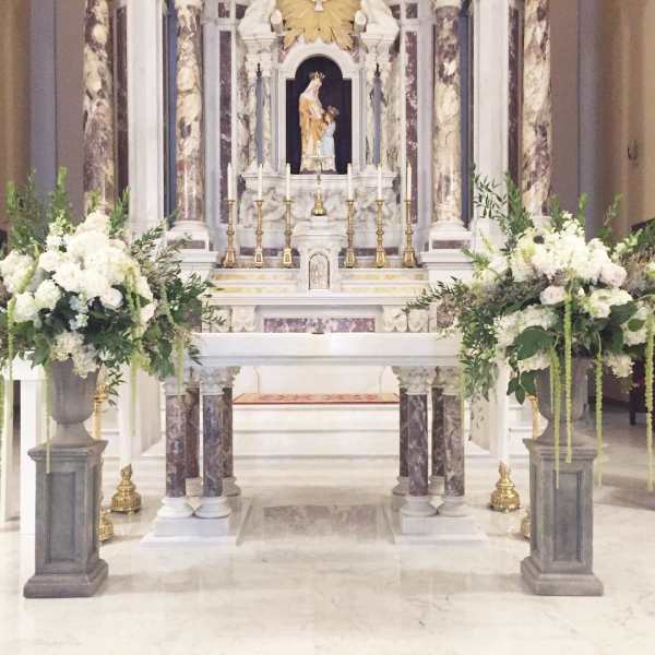 Large white floral altar arrangements flank a church altar with candles and a statue.