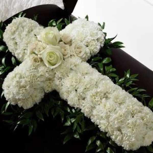 White floral cross arrangement with roses and carnations on a dark casket