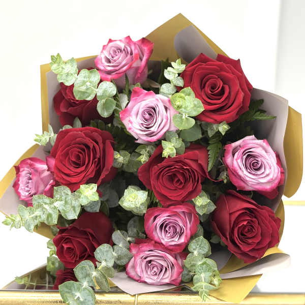 Bouquet of red and lavender roses wrapped in gold and white paper