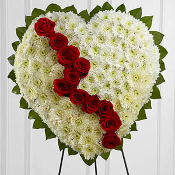 Heart-shaped floral tribute with white flowers and red roses on an easel