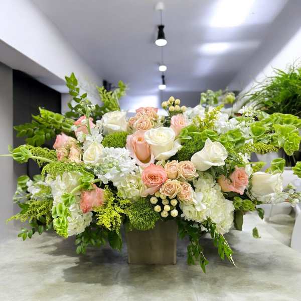 Large floral arrangement with white and blush roses in a square vase