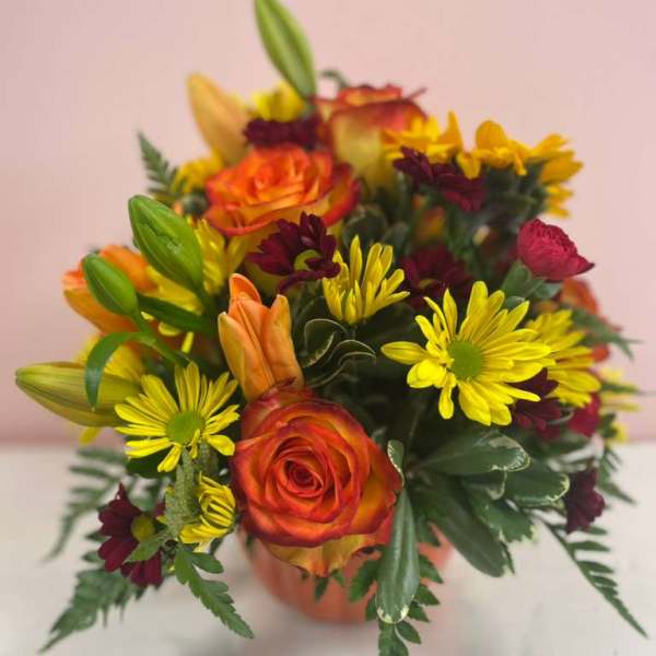 Mixed bouquet of orange roses, yellow daisies, and lilies in a vase