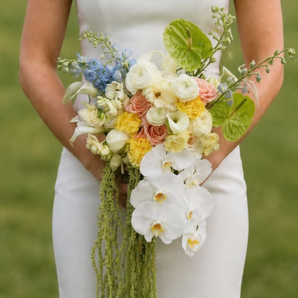 Bride holding a cascading bouquet of white, peach, yellow, and blue flowers