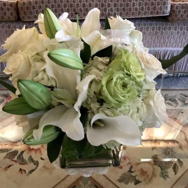White lilies and pale green flowers in a square glass vase