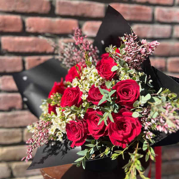 Bouquet of red roses with small white filler flowers in black wrap