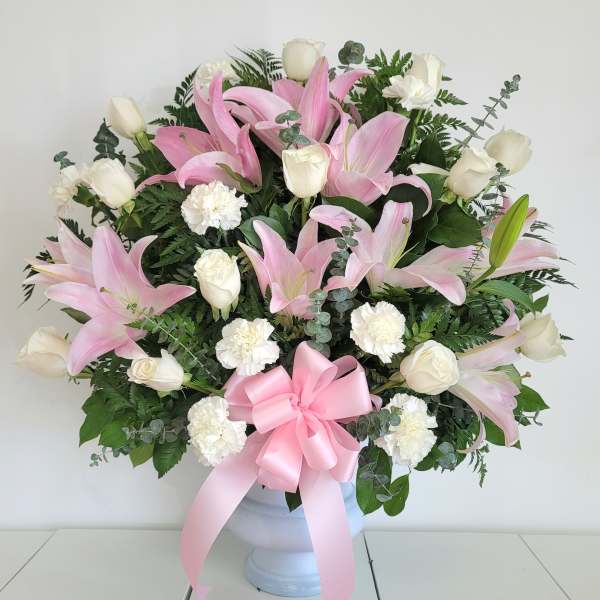 Pink lilies and white roses in a white vase with a pink ribbon