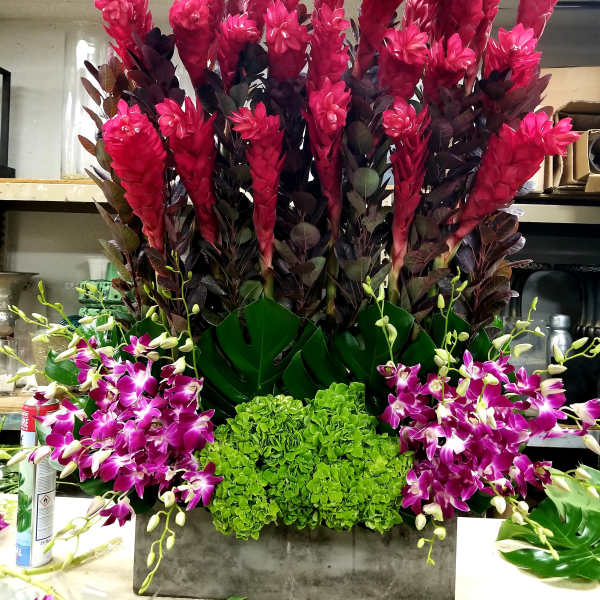 Tall floral arrangement with bright pink blooms, purple orchids, and green hydrangeas in a rectangular container