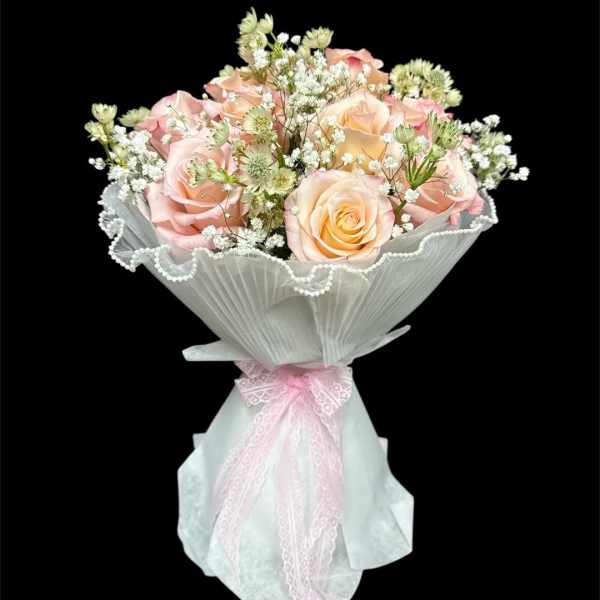 Bouquet of pale pink and peach roses wrapped in white paper with a pink ribbon