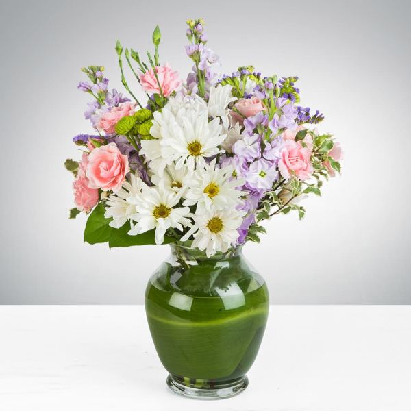 Mixed bouquet of white daisies, pink carnations, and lavender flowers in a green glass vase