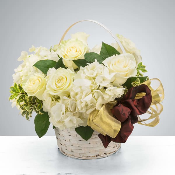 Cream roses and white hydrangeas in a woven basket with a ribbon bow.