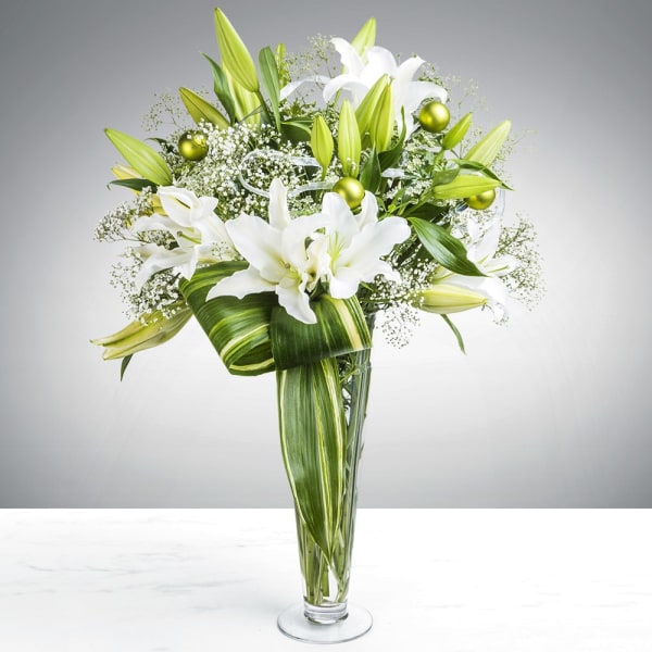 White lilies and green buds in a tall glass vase with green ribbon accents.