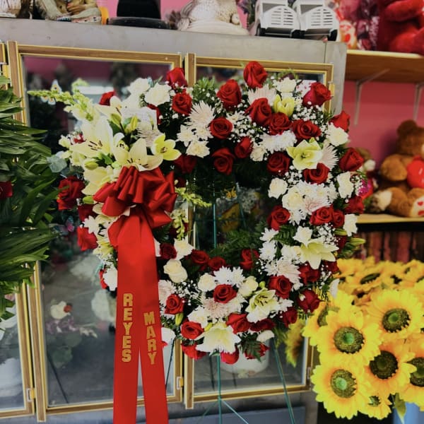 Heart-shaped wreath of red and white flowers on a stand with a red ribbon