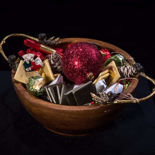 Wooden bowl filled with wrapped chocolates and a red glitter ornament