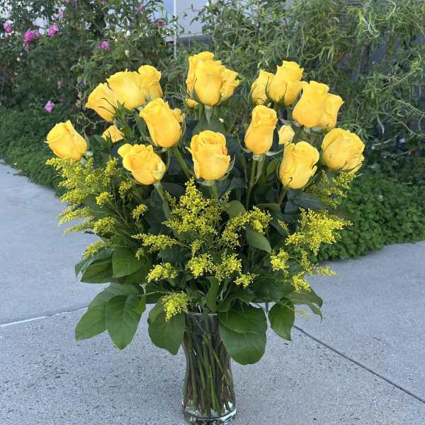 Yellow roses arranged in a clear glass vase with yellow filler flowers
