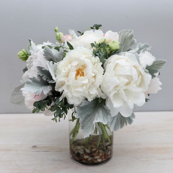Compact arrangement of white peonies in a glass vase with river stones.
