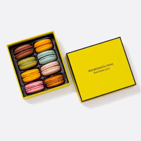 Box of colorful macarons with a yellow lid beside it