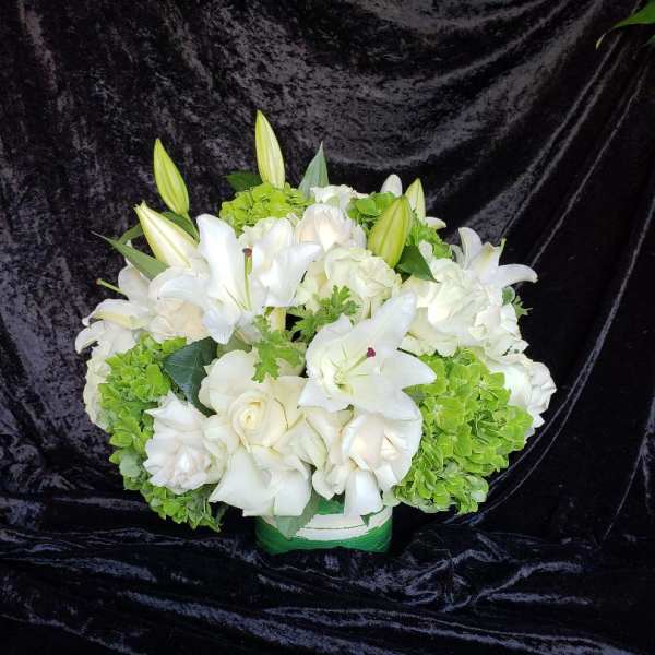 White lilies and roses arranged with green hydrangeas in a low container