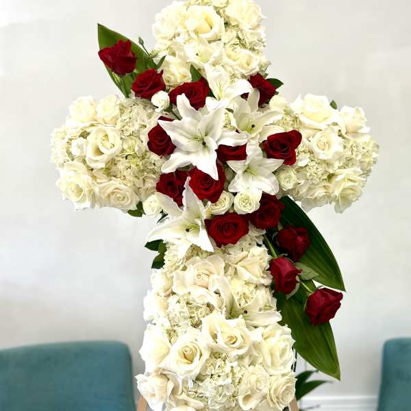 Cross-shaped floral arrangement of white hydrangeas, roses, lilies, and red roses