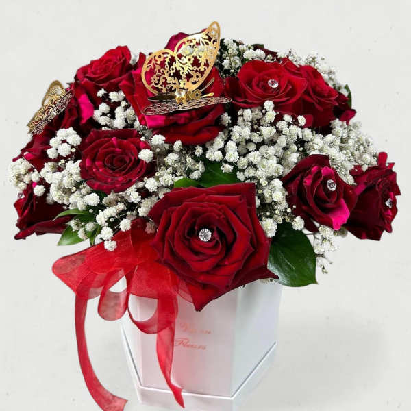 Red roses arranged in a white box with baby's breath and a red ribbon