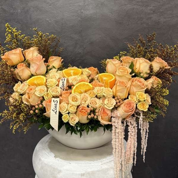 Peach and cream roses arranged in a white bowl with orange slices