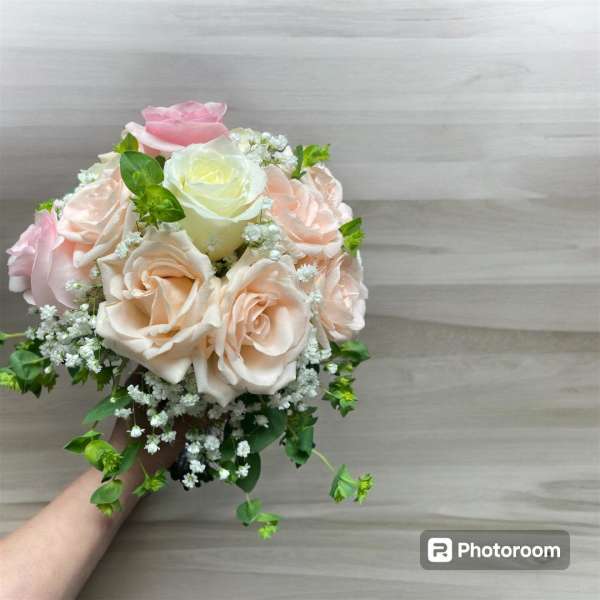 Handheld bouquet of pale pink and cream roses with small white filler flowers