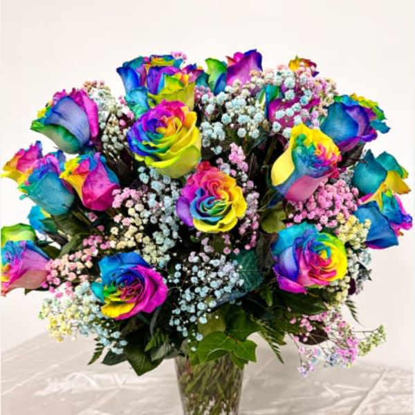 Rainbow-colored roses in a clear glass vase with baby's breath