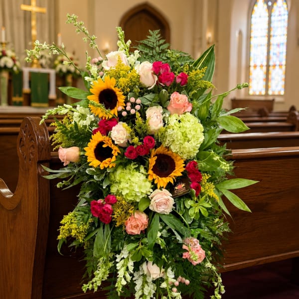 Large standing floral spray with sunflowers, roses, and hydrangeas in a church