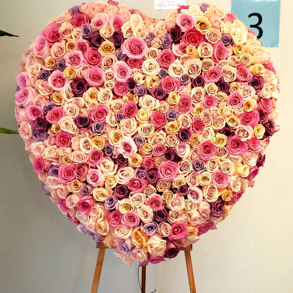 Heart-shaped rose arrangement on an easel in pink, peach, and purple tones