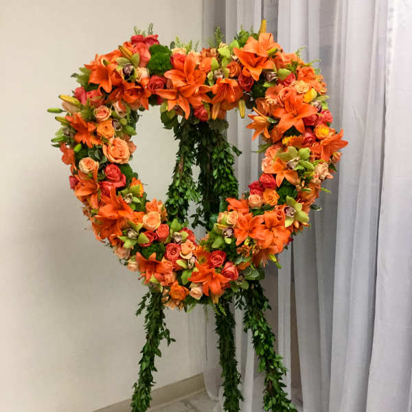 Heart-shaped floral wreath on a stand with orange and pink blooms