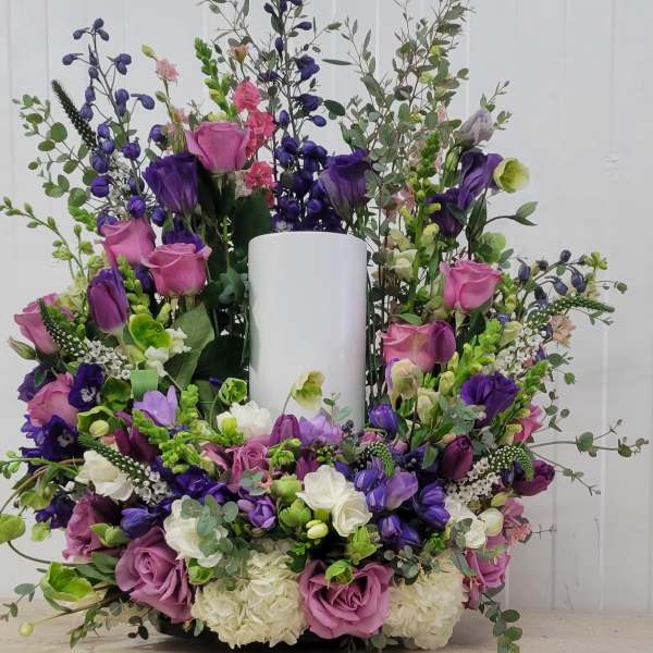 Large purple and pink floral arrangement around a white pillar candle