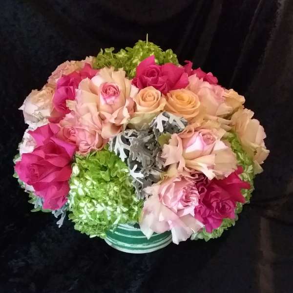 Bouquet of pink and peach roses with green hydrangeas in a striped vase