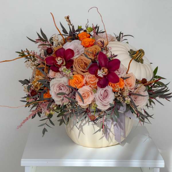 Floral arrangement in a white pumpkin container with roses and orchids