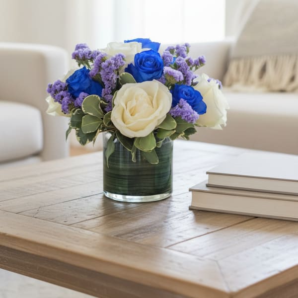 Blue and white roses in a glass vase with purple filler flowers