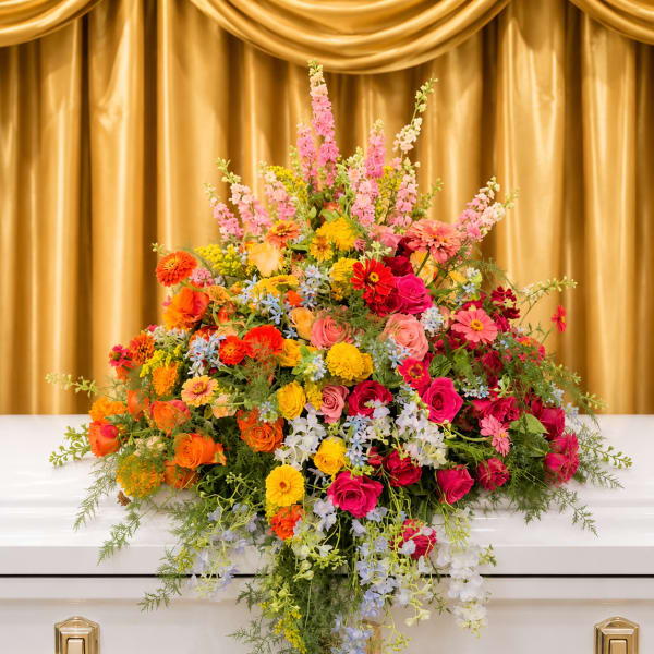 Colorful floral casket spray with roses, daisies, and snapdragons