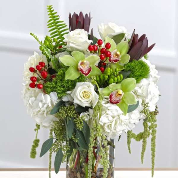 White roses and green orchids in a glass vase with red berries