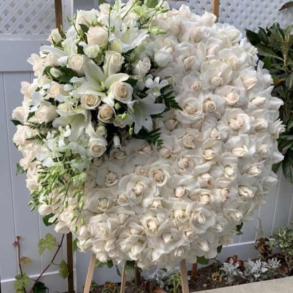 Large white floral wreath on an easel with roses and lilies