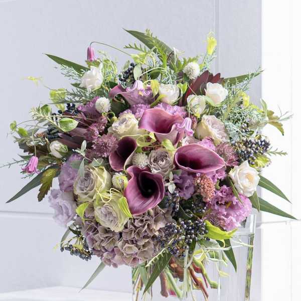 Bouquet of purple calla lilies, roses, and hydrangeas in a clear glass vase