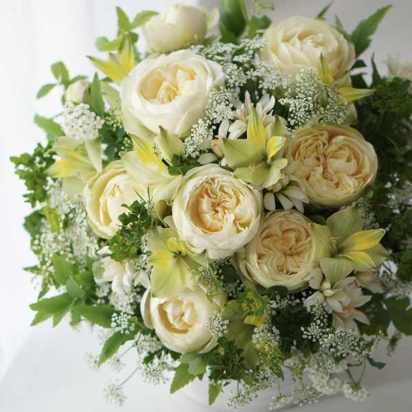 Cream roses and white flowers arranged in a white vase
